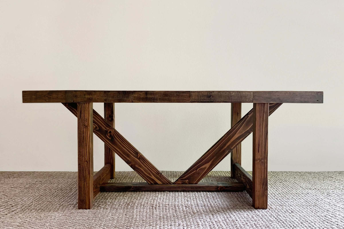 This handcrafted dining table features a thick reclaimed wood top and durable V-shaped legs, exemplifying enduring quality. Crafted in Arizona, it suits as a restaurant table or narrow bar-height table. Shown on a beige rug.