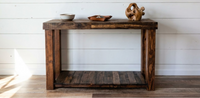 This handcrafted reclaimed wood console table, ideal as a narrow bar-height or entryway table, features enduring craftsmanship with a lower shelf. Styled on a white shiplap wall, it elevates any space with sustainable quality.