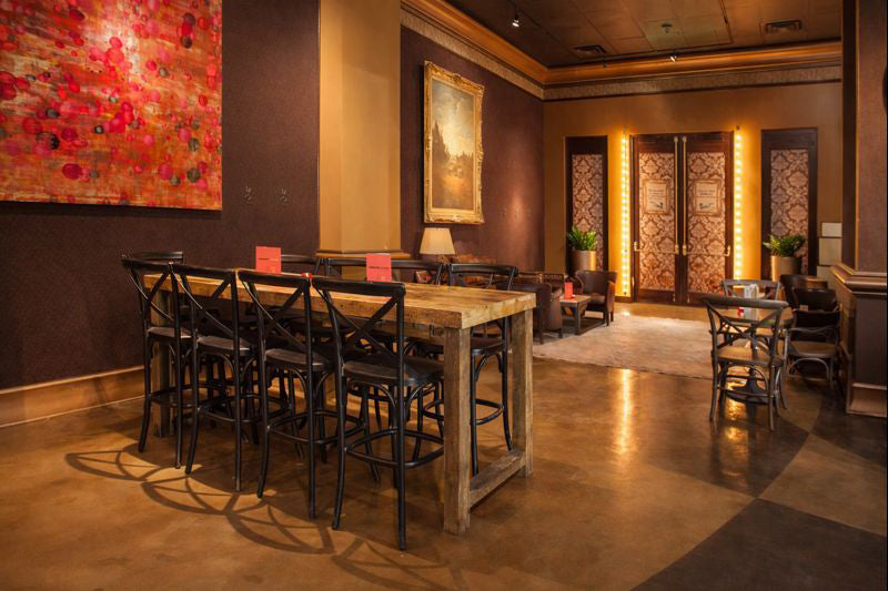 A welcoming lounge with warm lighting highlights a handcrafted reclaimed wood bar-height table paired with sleek black chairs. Accented by cozy armchairs, vibrant plants, wall art, and refined decor for lasting style.