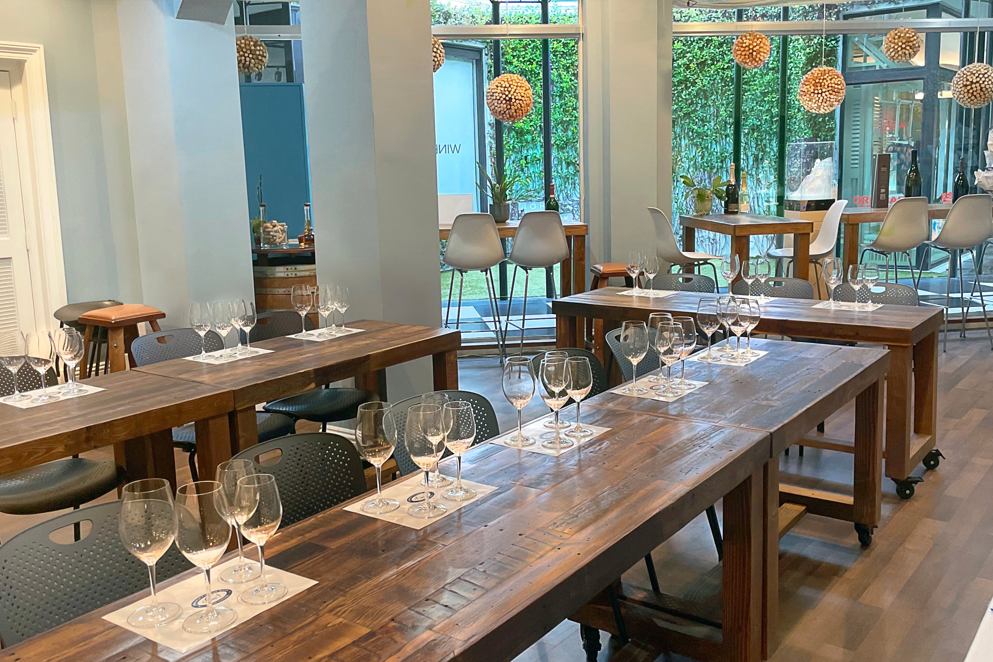 A bright, modern wine tasting room showcases U-shaped solid wood dining tables and a handcrafted reclaimed wood bar-height table by expansive windows. Bar stools highlight the enduring quality of our Arizona-made furniture.