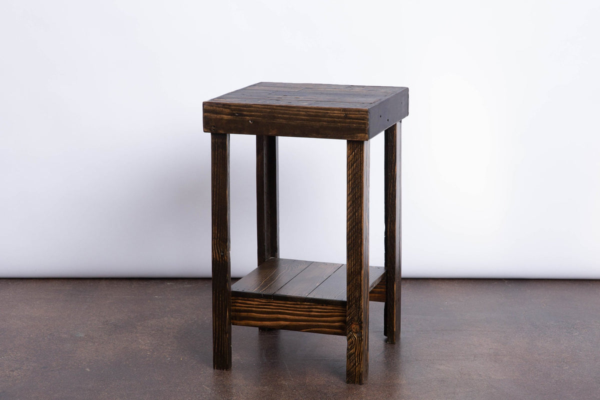 This handcrafted reclaimed wood side table showcases timeless craftsmanship, featuring a dark-stained square top, four straight legs, and a lower shelf. Ideal as a narrow bar-height or kitchen island accent.