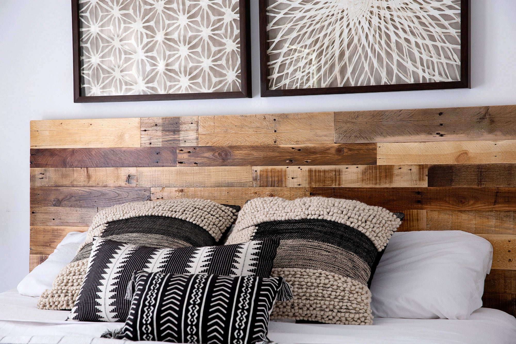 Handcrafted bed with reclaimed wood headboard, black and beige patterned decorative pillows, and two framed geometric wall art pieces; ideal for modern or minimalist bedrooms.