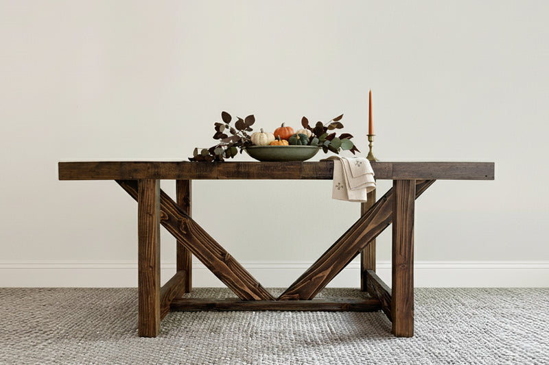 Handcrafted in Arizona, this reclaimed wood farmhouse dining table embodies enduring quality. The dark finish highlights expert craftsmanship, accented by autumnal décor and a light cloth, perfect for home or restaurant settings.