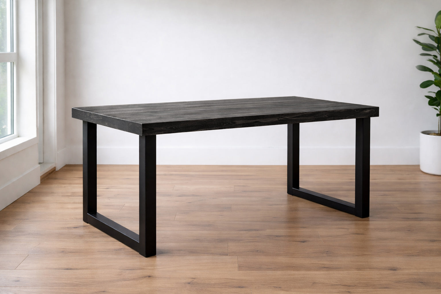 Reclaimed black wood modern dining table with sleek black metal legs in a room with a window and plant. Rustic, natural and modern. Sustainably made by Kase Custom in Arizona. 