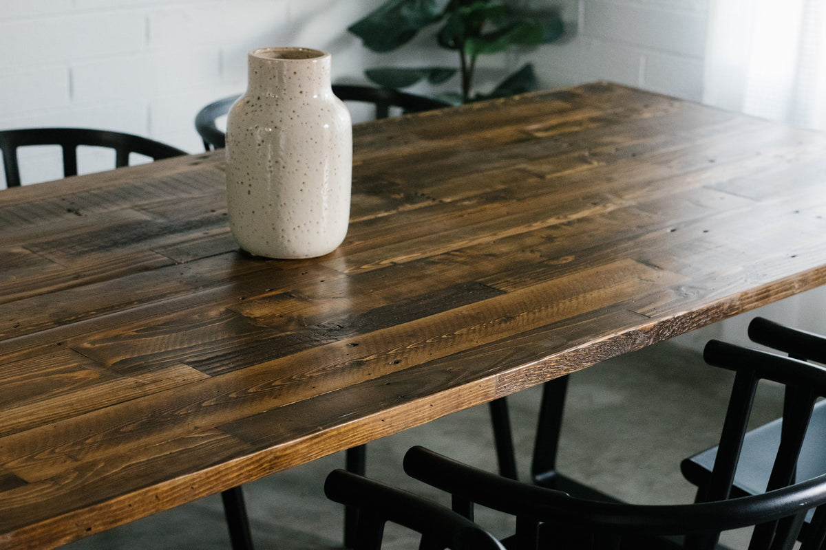 A reclaimed wood dining table surrounded by sleek black chairs. This artisan-crafted piece features sustainable materials and enduring quality, perfect for modern spaces with natural light.