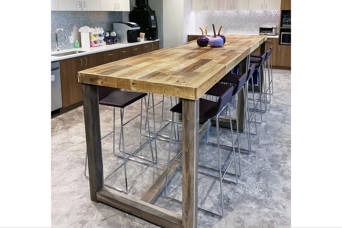 Office breakroom table is handcrafted reclaimed wood bar height table, paired with sleek high stools and accented by two purple vases. This Arizona-made reclaimed wood furniture features warm wood cabinets and a tiled backsplash for lasting quality and great co-working space.