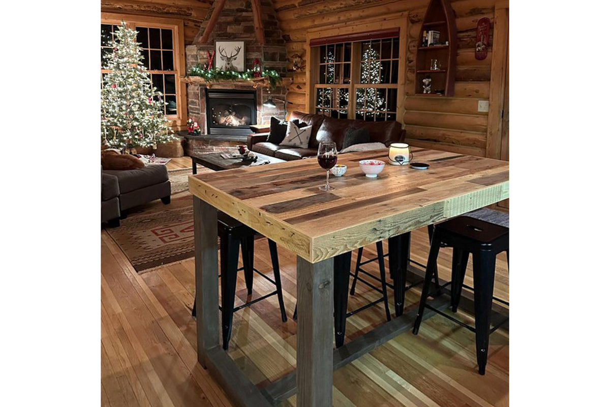 A warm log cabin interior with festive decor features a handcrafted reclaimed wood Sequoia dining-height bar table. Expertly made in Arizona, this sustainable table reflects enduring quality and design.