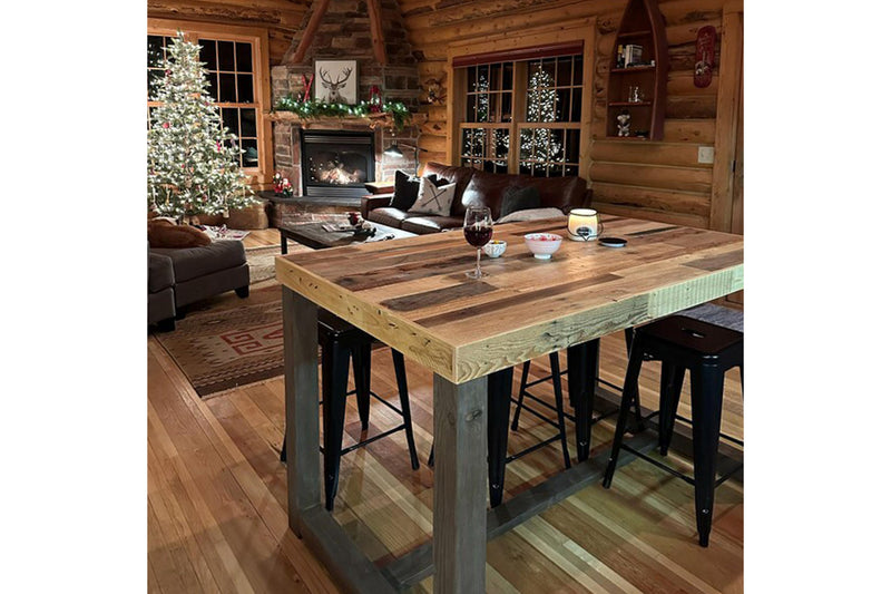 Wooden counter height dining table in a cozy log cabin living room with Christmas decorations.