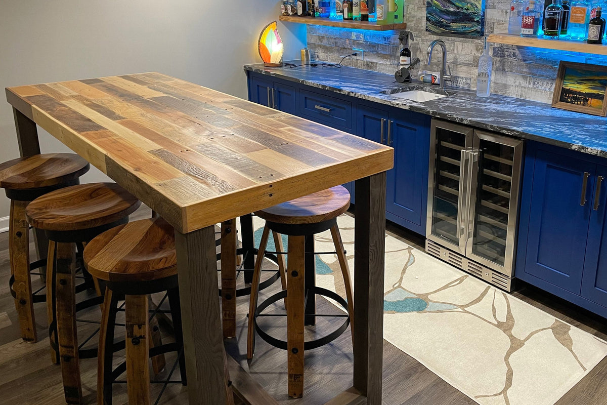 Elevate your space with a handcrafted Sequoia bar table and four matching stools, expertly built from reclaimed wood in Arizona. This durable piece anchors a modern home bar basement space with blue cabinets, marble counters, and curated shelving.