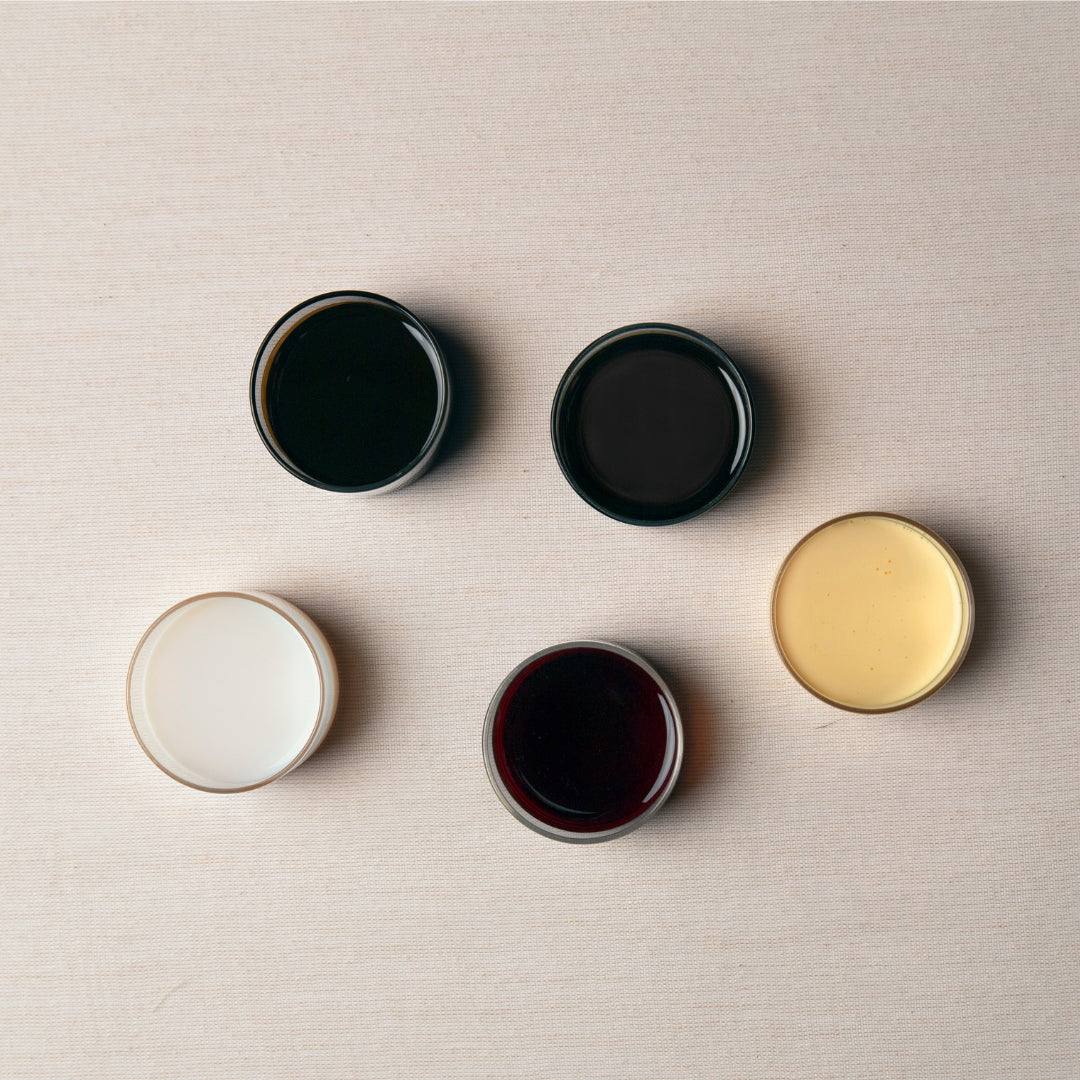 A set of five artisan glass bowls, each filled with a distinctively colored liquid, thoughtfully arranged in a circle on a reclaimed wood kitchen island. Handcrafted in Arizona for exceptional quality and lasting beauty.