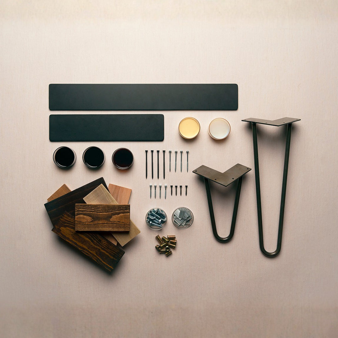 A thoughtfully organized DIY kit for a reclaimed wood bar-height table includes sturdy steel legs, sustainable wood samples in assorted finishes, hardware, paint cans, and durable black panels—crafted to last.