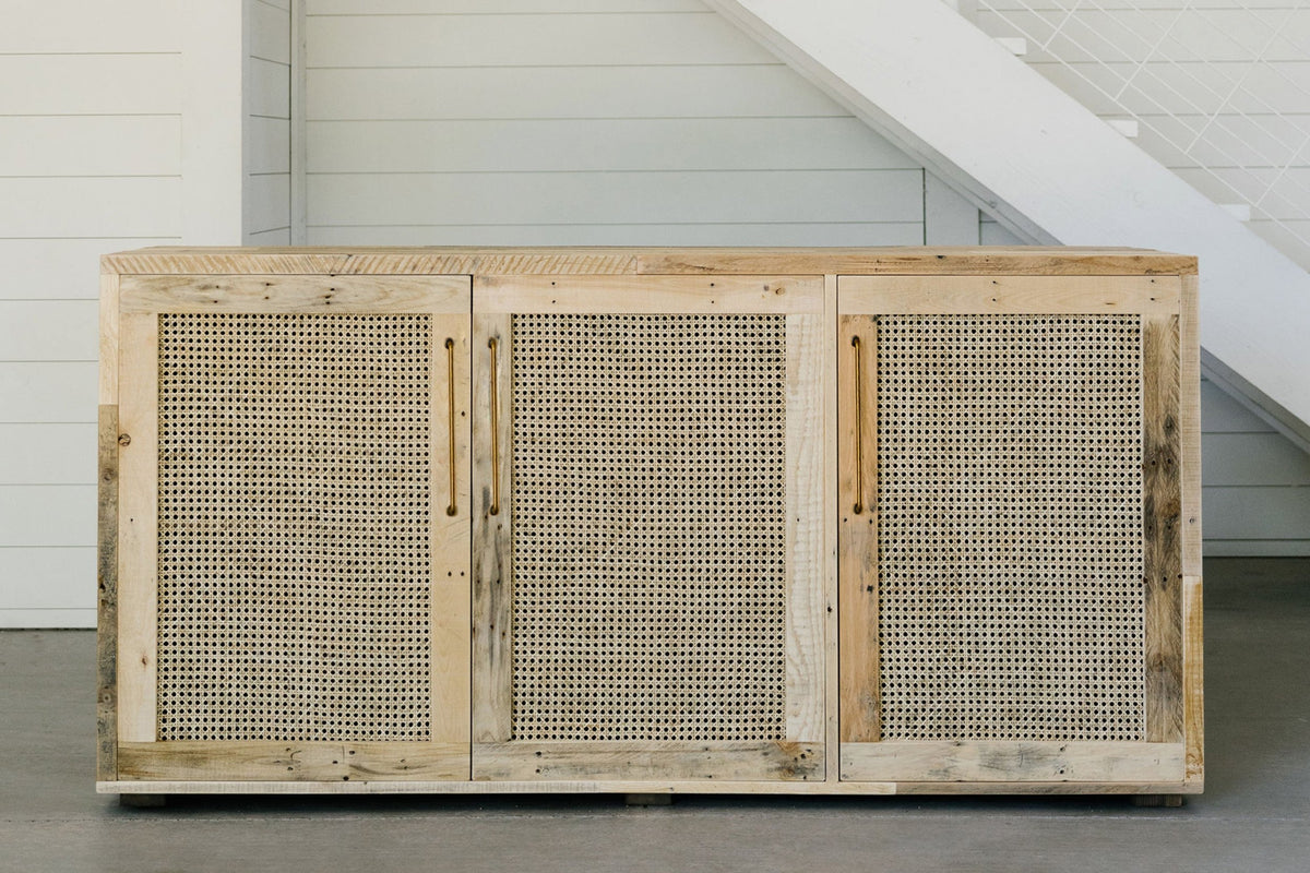 Expertly crafted from reclaimed wood, this sideboard features three woven rattan doors—coastal traditional style storage.