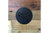 Round black power outlet with two standard sockets and two USB ports, installed on reclaimed wood surface; ideal for modern café tables, minimalist workspaces, or eco-friendly bar-height dining furniture.