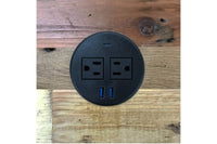 Round black power outlet with two standard sockets and two USB ports, installed on reclaimed wood surface; ideal for modern café tables, minimalist workspaces, or eco-friendly bar-height dining furniture.